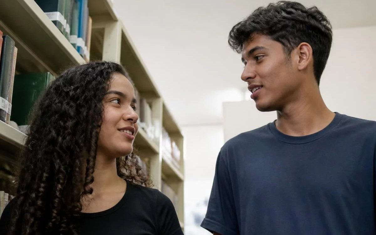 Três pessoas sentadas a uma mesa comprida, no meio de uma conversa numa sala de janelas altas